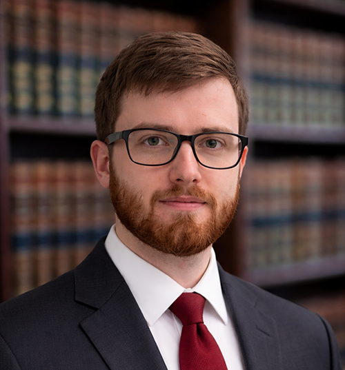 Professional headshot of Joseph Biancarosa facing camera wearing a suit in front of bookshelves